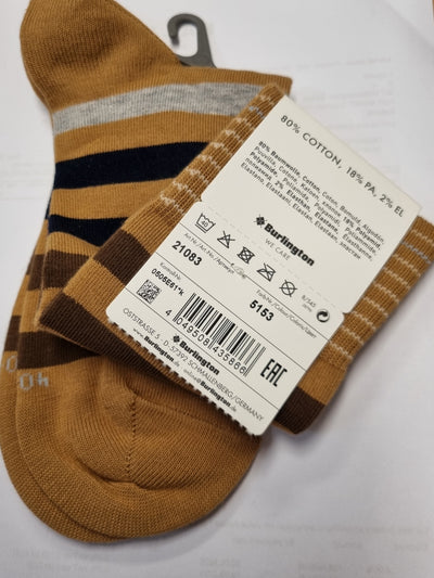 A pair of Burlington ankle socks in brown, beige, and navy blue stripes, shown with their paper product tag on a white sheet of paper over a wooden table.
