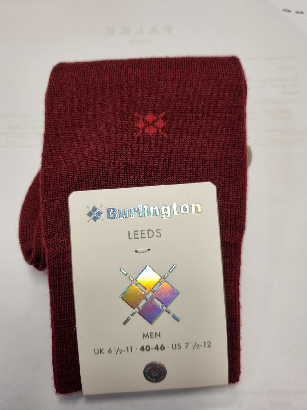 A folded pair of burgundy knit socks with a small red embroidered logo, attached to a white paper tag that reads 'Burlington LEEDS MEN'.