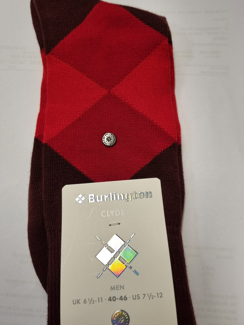 A single folded Burlington Clyde men's sock with an argyle pattern in red and dark brown, featuring a small silver button and a paper tag attached.