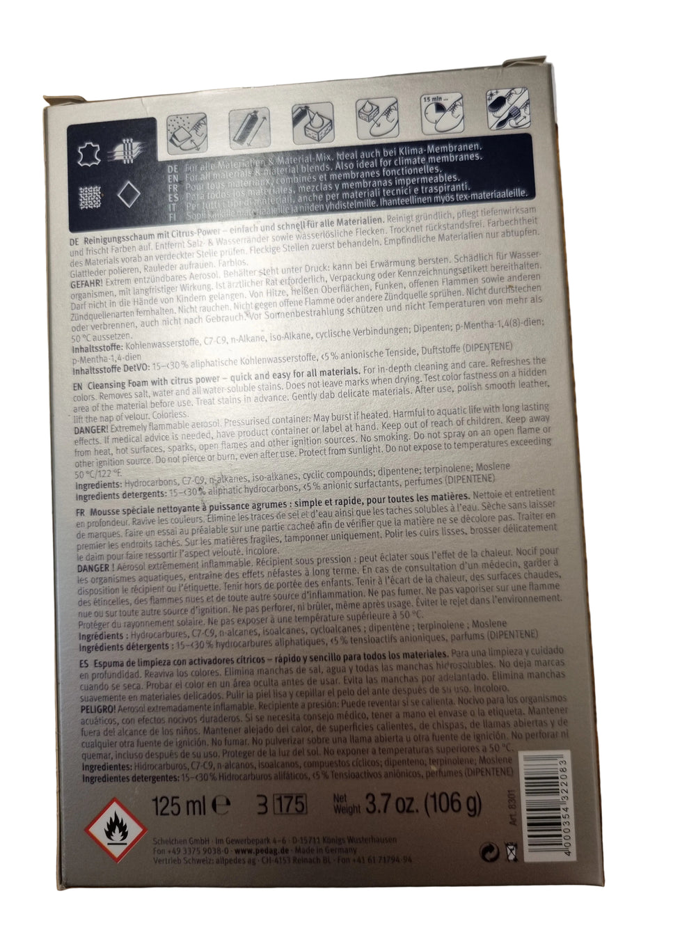 The back of a rectangular product box photographed from above on a wooden tabletop. The box has a dark gray to black label with white text, icons, and a barcode, and a small red hazard symbol near the bottom left.