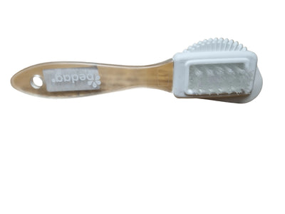 A Pedal baby grooming brush with a clear plastic handle and a white bristle head, resting on a wooden tabletop.